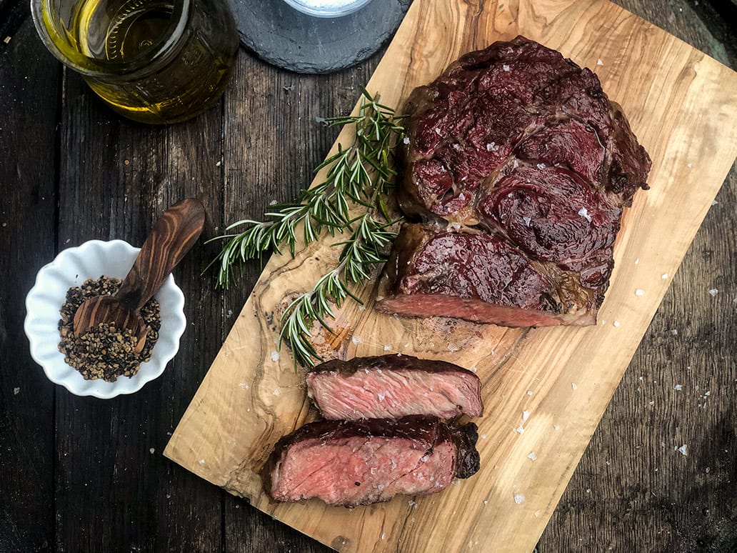 Entrecôte/Rib-Eye Saftiges, medium gegrilltes Rindersteak, aufgeschnitten auf einem rustikalen Holzbrett mit Rosmarin und Gewürzen angerichtet.