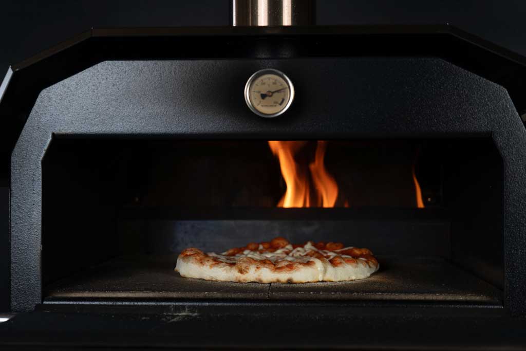 Pizza backt auf Steinplatte im MERKLINGER Holzbackofen vor lodernder Flamme