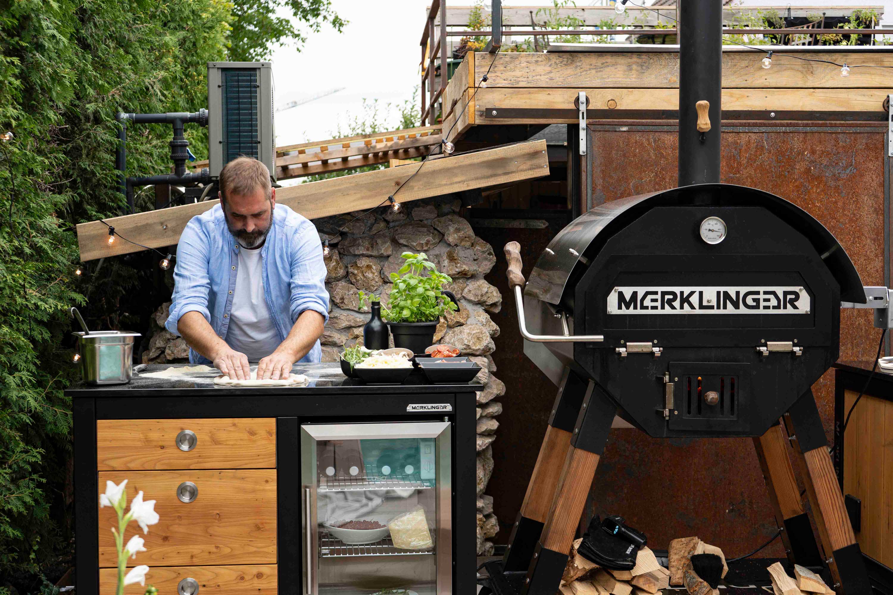 Merklinger Mann bereitet Teig am Outdoor-Küchenmodul mit Glastür-Kühlschrank neben MERKLINGER Holzbackofen