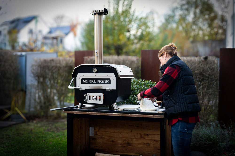Frau knetet Pizzateig auf schwarzer Granitarbeitsfläche neben MERKLINGER Ofen.