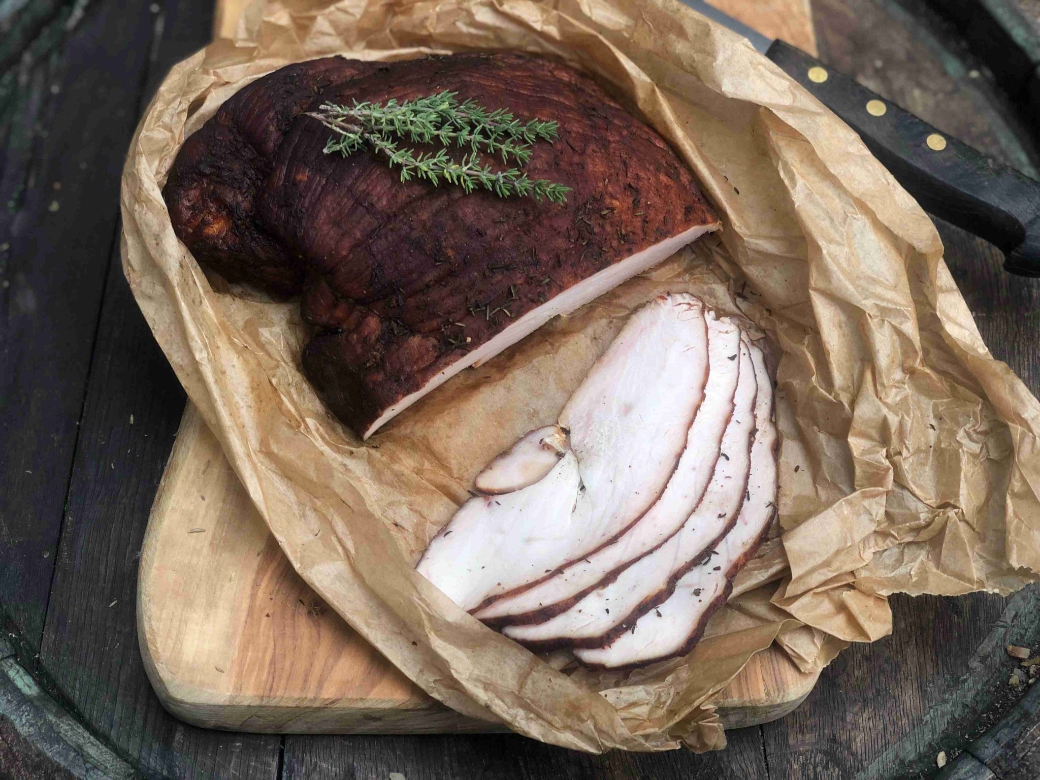 Fein aufgeschnittene, geräucherte Putenbrust auf Backpapier, dekoriert mit Thymian auf einem Holzbrett.