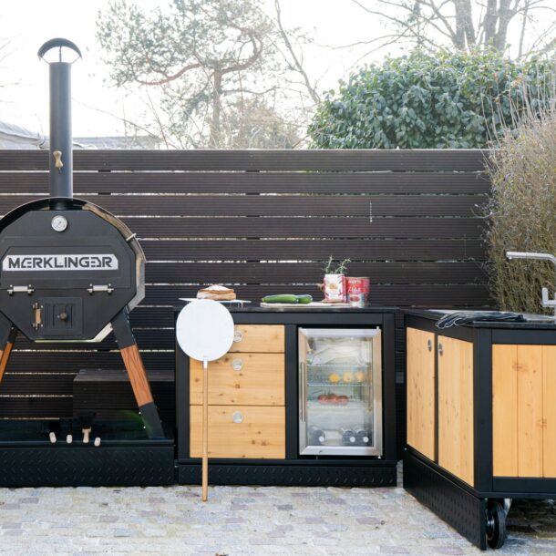 MERKLINGER Outdoor-Küche im Garten mit Holzbackofen, Kühlschrankmodul mit Glastür und Spül/Arbeitsmodul.“