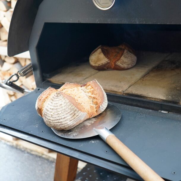 Brotschieber auf Ablage – Backen auf Stein „Brotschieber mit rundem Laib auf der Ablage, zweites Brot im MERKLINGER Ofen auf Stein.“