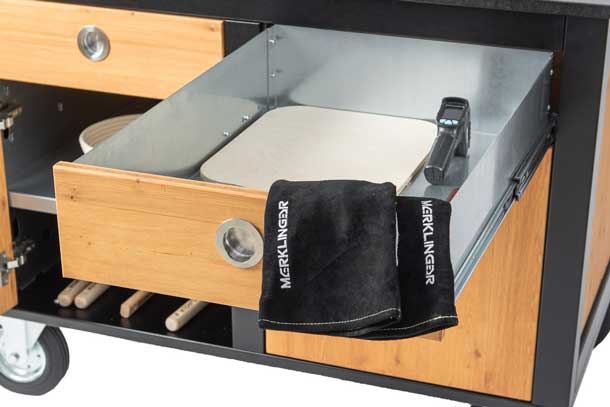 Geöffnete Schublade des MERKLINGER Wagens mit Pizzastein, Infrarot-Thermometer und MERKLINGER Handschuh.