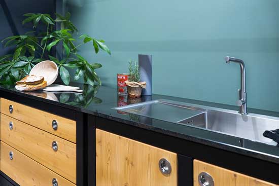 Spülbereich mit Granitplatte und Edelstahlbecken; Kräuter und Zutaten daneben.