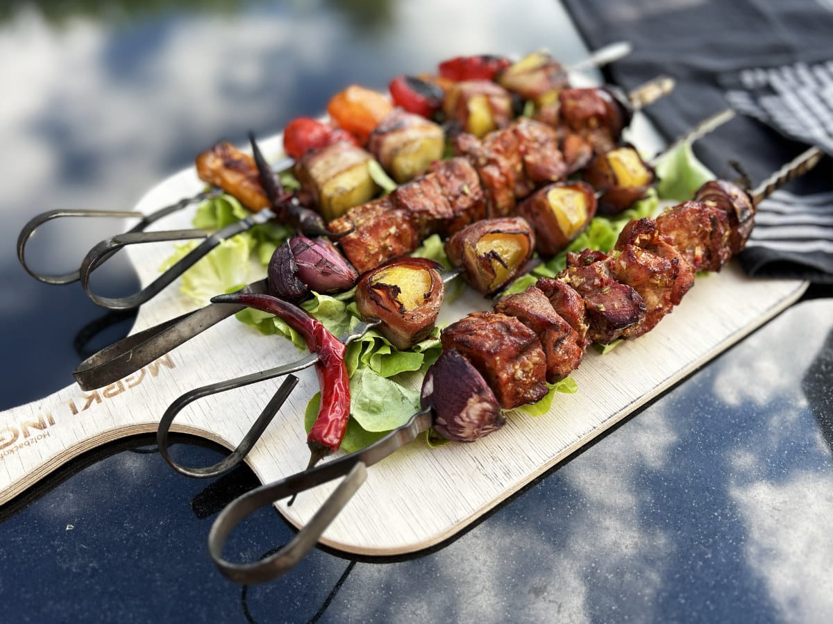 Verschiedene bunte Fleischspieße mit Gemüse, frisch gegrillt und angerichtet auf einem Holzbrett mit Salat und Chili.