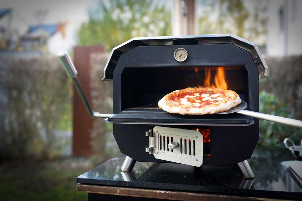 Pizza wird mit Schaufel aus brennendem MERKLINGER Holzbackofen genommen