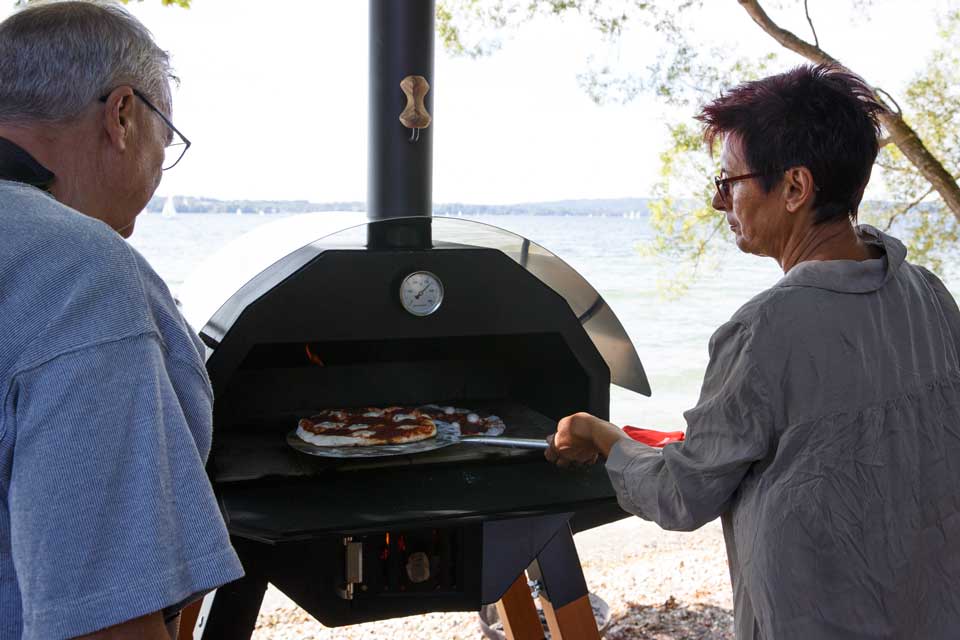 Paar backt Pizza am See Älteres Paar backt gemeinsam Pizza im MERKLINGER Tischofen am Seeufer