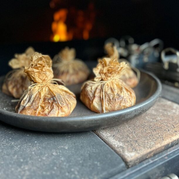 Im heißen Ofen liegende runde Platte mit kleinen, zu Päckchen gebundenen Backpapier-Beuteln; dahinter flackert die Flamme Im heißen Ofen liegende runde Platte mit kleinen, zu Päckchen gebundenen Backpapier-Beuteln; dahinter flackert die Flamme. Merklinger Zubehör Denkkeramik Keltenschale 03
